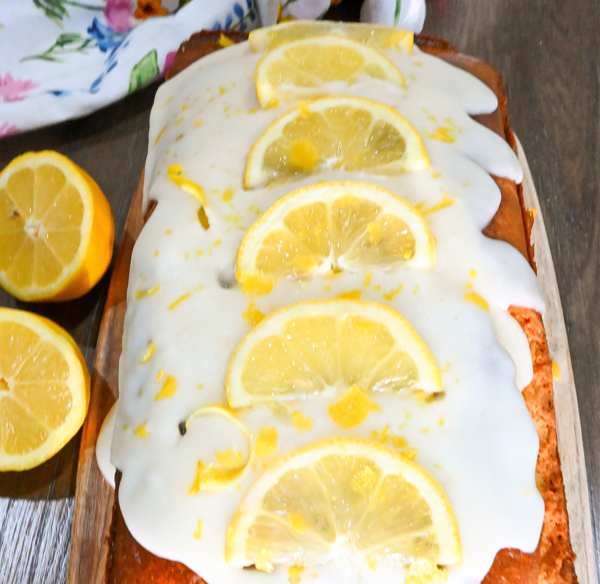 keto lemon cake with slices of lemon and lemon zest on top of lemon tangy icing
