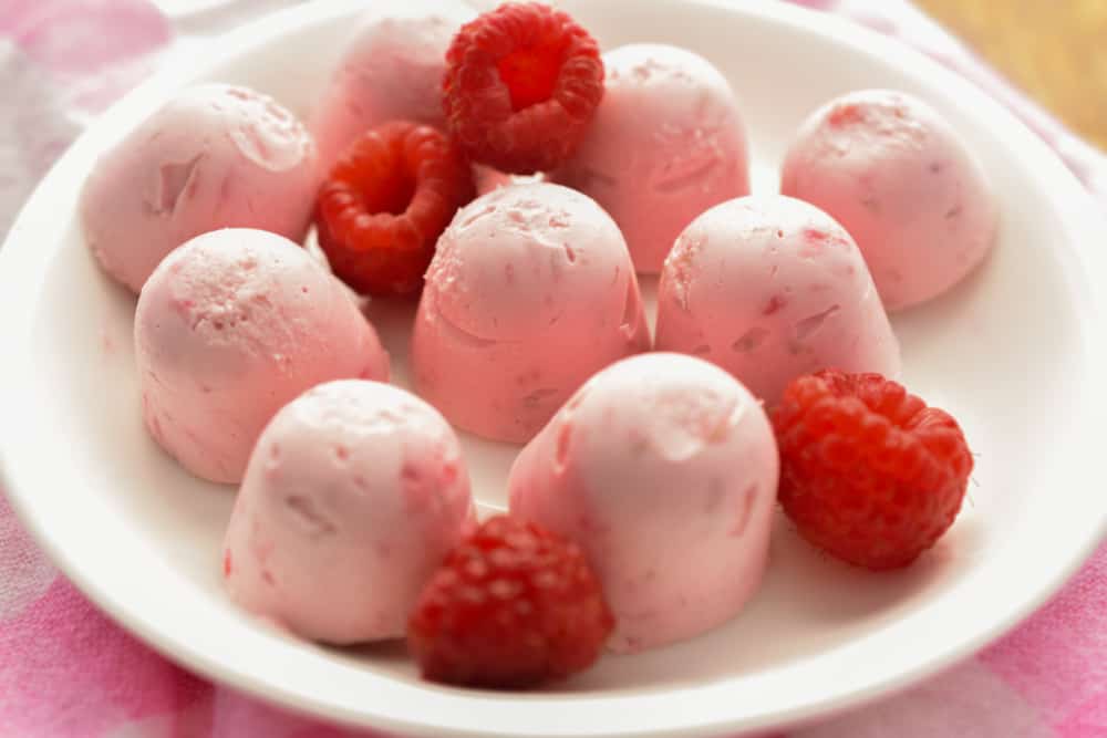 Raspberry Cheesecake Fat Bombs on White Plate with Scattered Raspberries