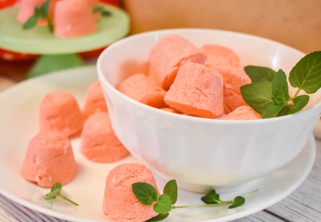 strawberry jello cream cheese fat bombs in white bowl and white plate with mint leaves and green pedestal in background