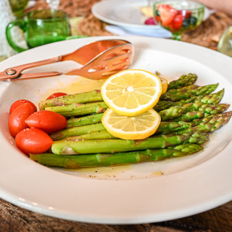 keto asparagus salad served on white platter topped with lemon slices and tomatoes up close