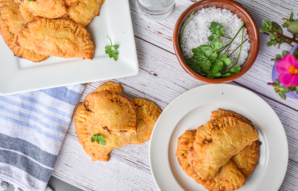 keto ground beef empanadas on white plates and on table with blue towel and dish filled with salt and herbs