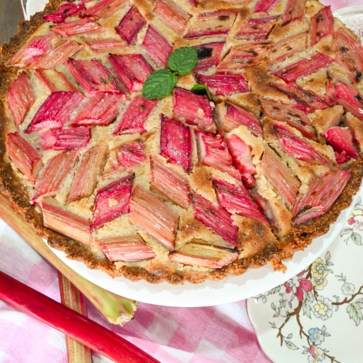 keto rhubarb tart on cake stand with rhubarb stalks next to it