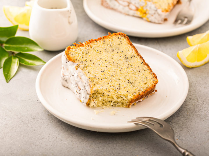 keto poppy lemon seed cake slice on a small white plate with lemon wedges next to it