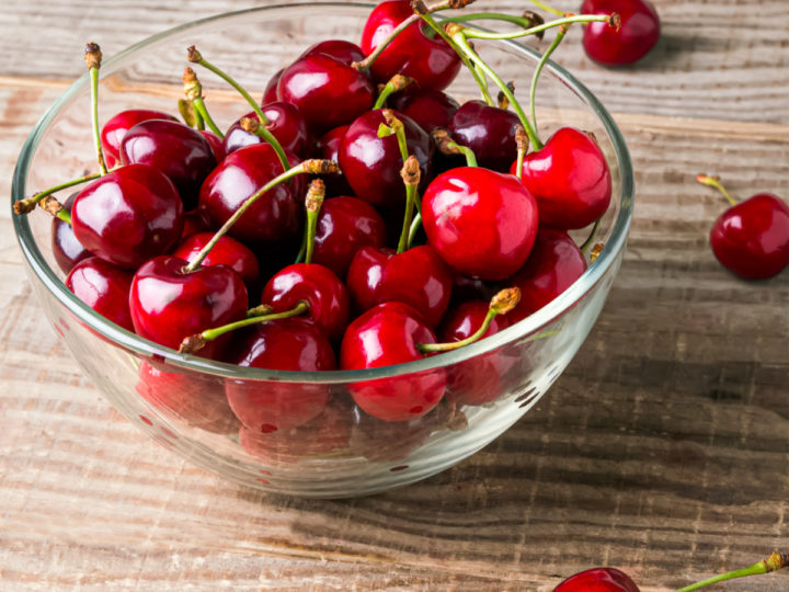 bowl of fresh cherries in a clear bowl on a wooden table