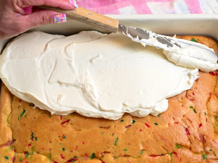 funfetti keto cake being frosted with a keto cream cheese frosting