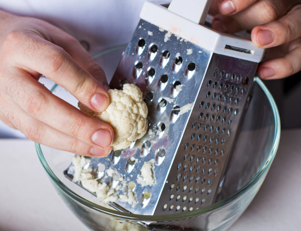 Raw cauliflower being riced use a box grater