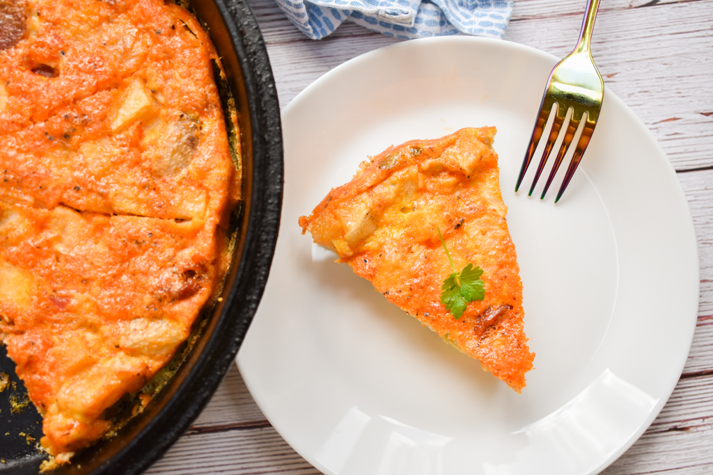 keto frittata in cast iron skillet with slice serve on white plate close up