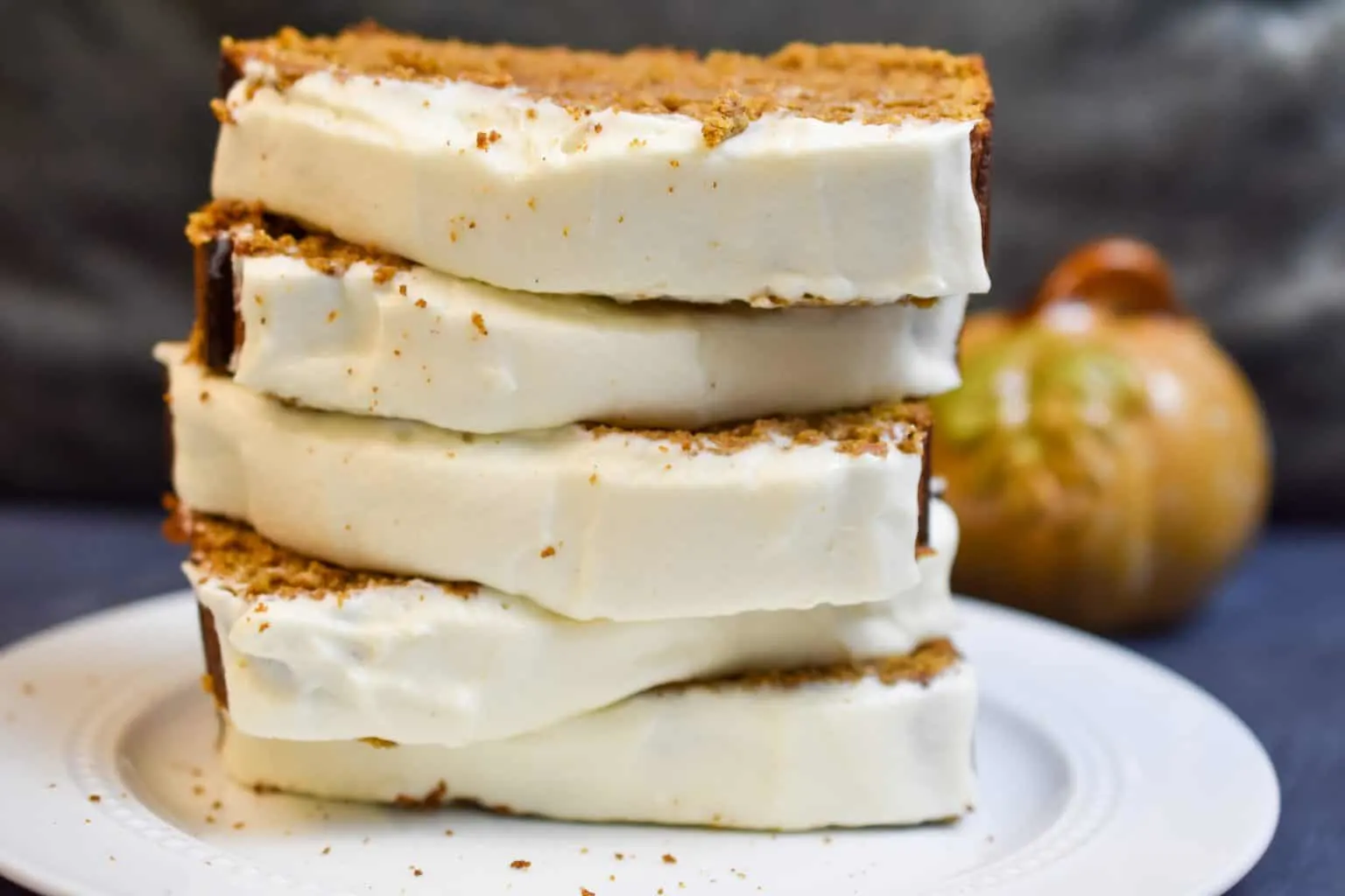 keto pumpkin bread with frosting stacked on a white pate