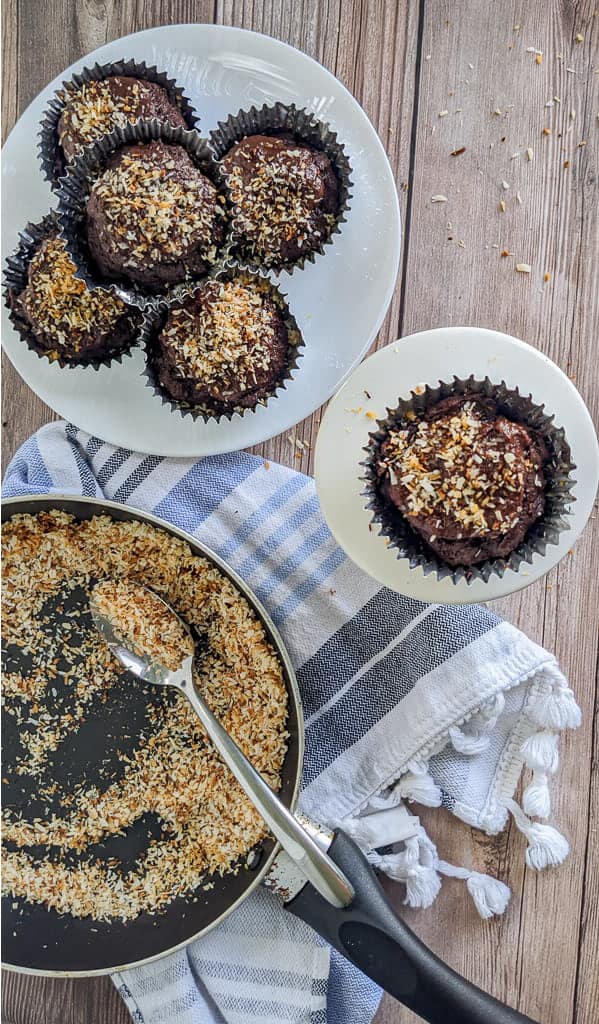 keto chocolate toasted coconut cupcakes on white plates on a wood background