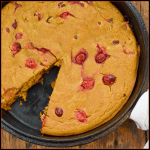 keto pumpkin cranberry cake on wood board with a slice missing