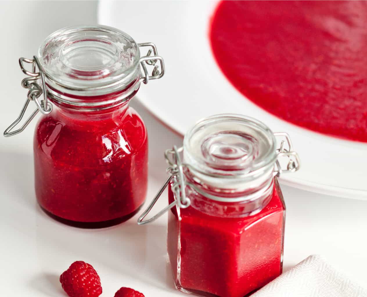 low carb raspberry curd in small mason jars and a large bowl featured.