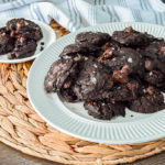 keto fudge flourless cookies on white plate and brown mat with striped towel in background