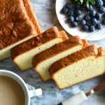 Keto coconut flour pound cake sliced on a marble slab with blueberries next to it