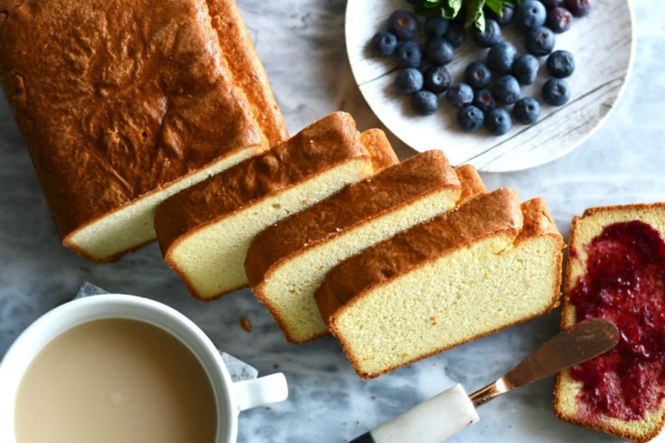 Keto coconut flour pound cake sliced on a marble slab with blueberries next to it