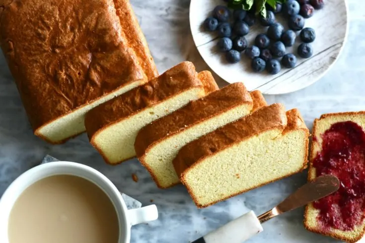 Keto coconut flour pound cake sliced on a marble slab with blueberries next to it