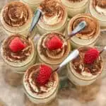 individual keto tiramisu cheesecakes with spoons and raspberries in glass mini mason jars