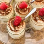 upclose individual keto tiramisu cheesecakes with spoons and raspberries on a wood board