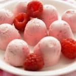 Raspberry Cheesecake Fat Bombs on White Plate with Scattered Raspberries