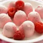 Raspberry Cheesecake Fat Bombs on White Plate with Scattered Raspberries