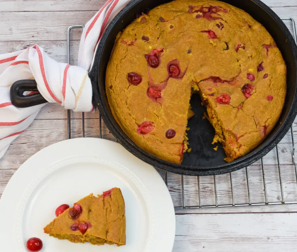 easy keto pumpkin cranberry skillet cake on cooling rack with a slice on a white plate