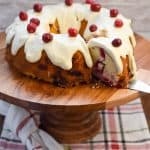 Keto Christmas cranberry cake on wood cake stand being sliced