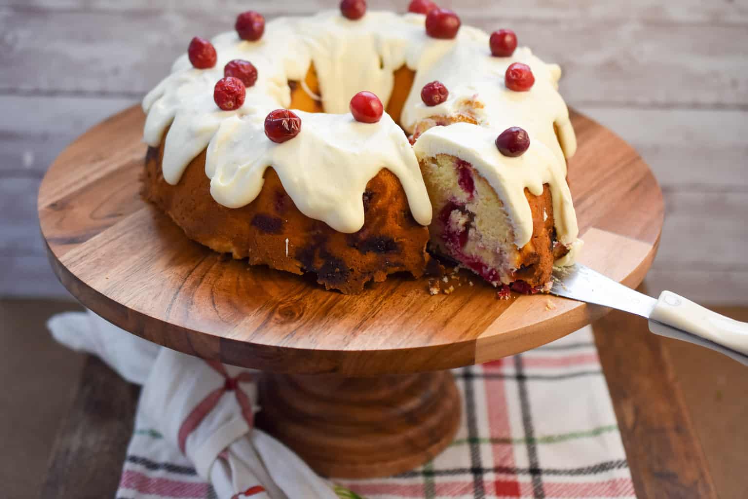 Keto Christmas cranberry cake on wood cake stand being sliced