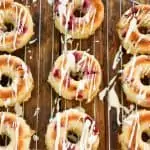 keto cranberry donuts on a baking rack being iced with vanilla icing
