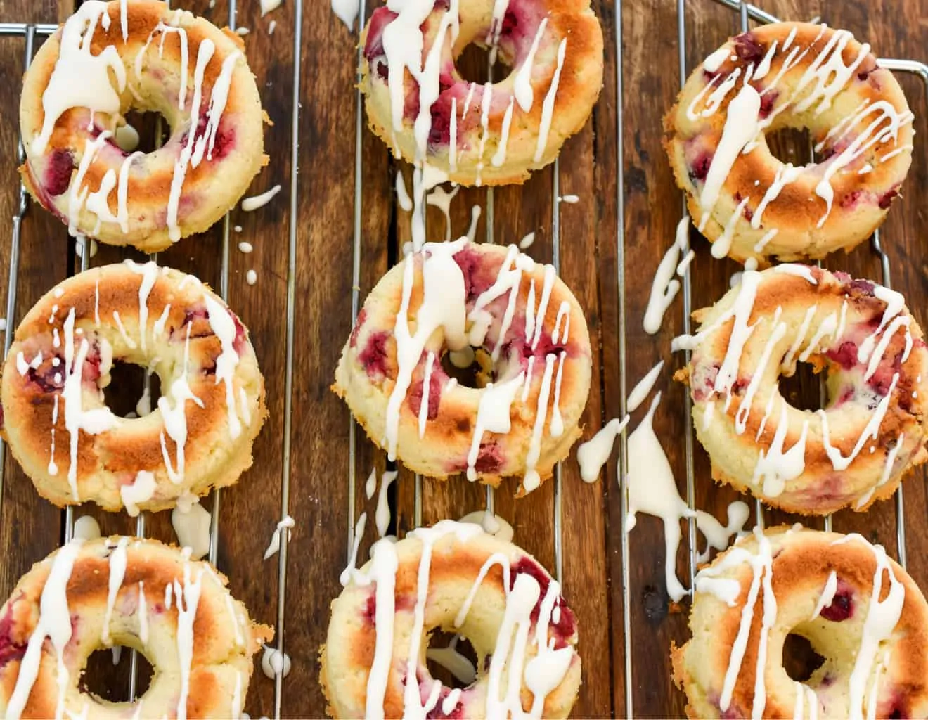 keto cranberry donuts on a baking rack being iced with vanilla icing