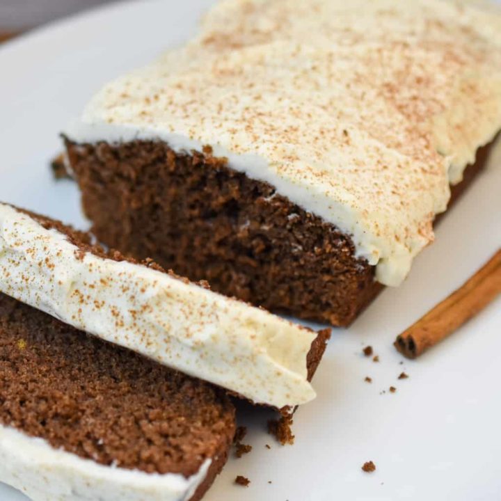 keto gingerbread loaf with cream cheese icing on a large white platter partially sliced