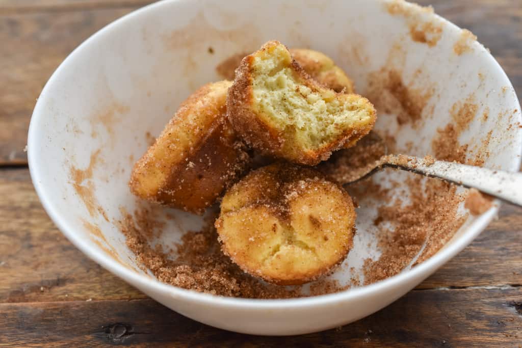 keto mini churros with a bite in white bowl of cinnamon sugar