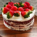 Keto red velvet cake on a wooden cake stand topped with fresh strawberries