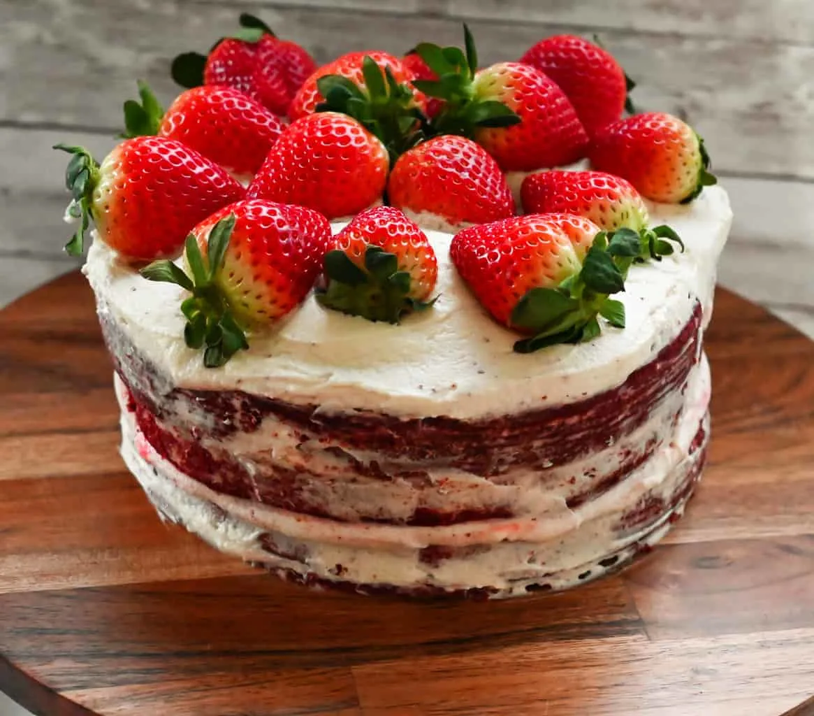 Keto red velvet cake on a wooden cake stand topped with fresh strawberries