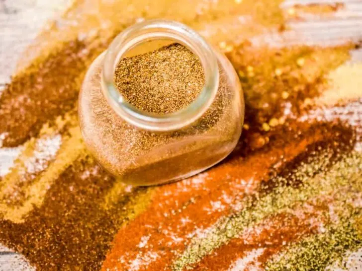 keto tex mex seasoning in a glass jar with spices spread all over surface