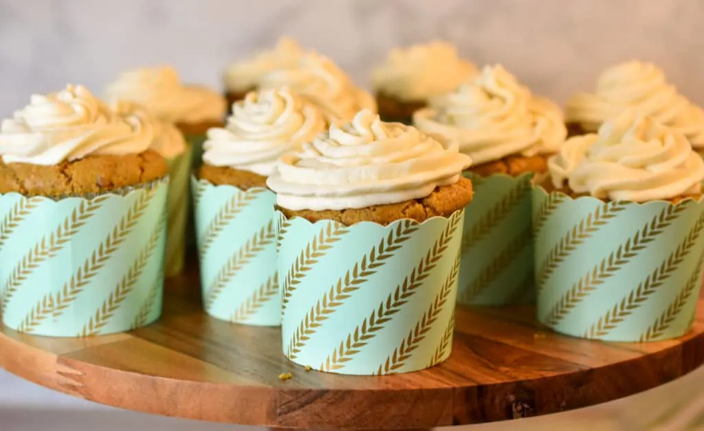 keto carrot cupcakes with cream cheese frosting on a wood cake stand