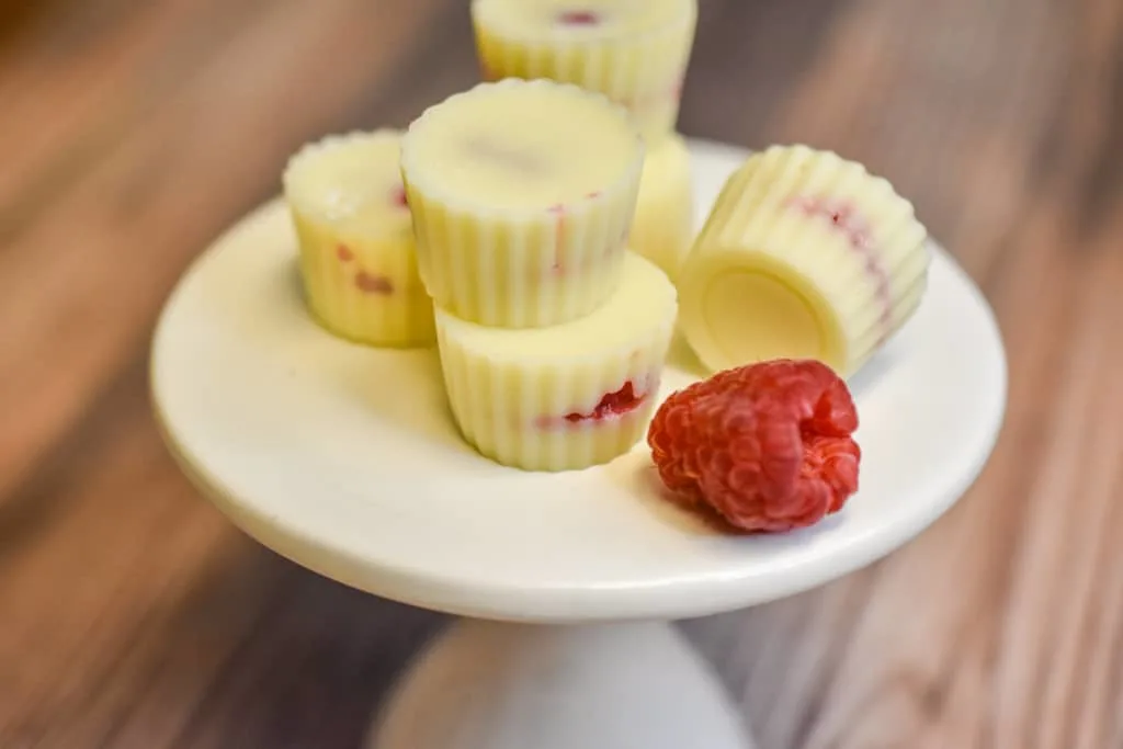 white chocolate raspberry fat bombs on a white pedestal stand