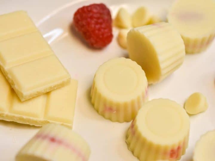 white chocolate raspberry fat bombs on a white plate with raspberries and chocolate bars