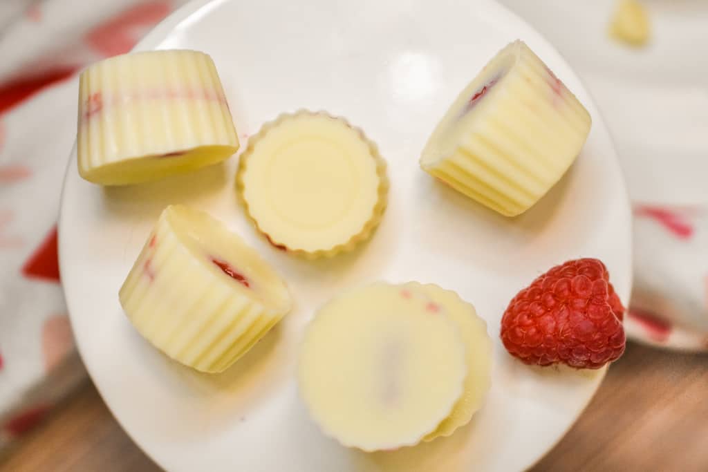 white chocolate raspberry fat bombs on white background with a fresh raspberry