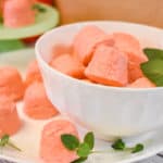 strawberry jello cream cheese fat bombs in white bowl and white plate with mint leaves and green pedestal in background