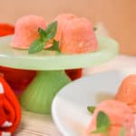 strawberry jello cream cheese fat bombs on green pedestal with mint leaves and red polka dot towel
