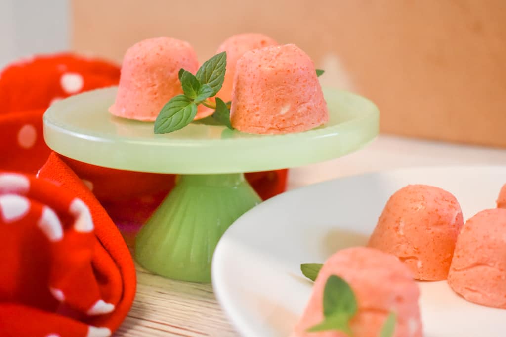 strawberry jello cream cheese fat bombs on green pedestal with mint leaves and red polka dot towel