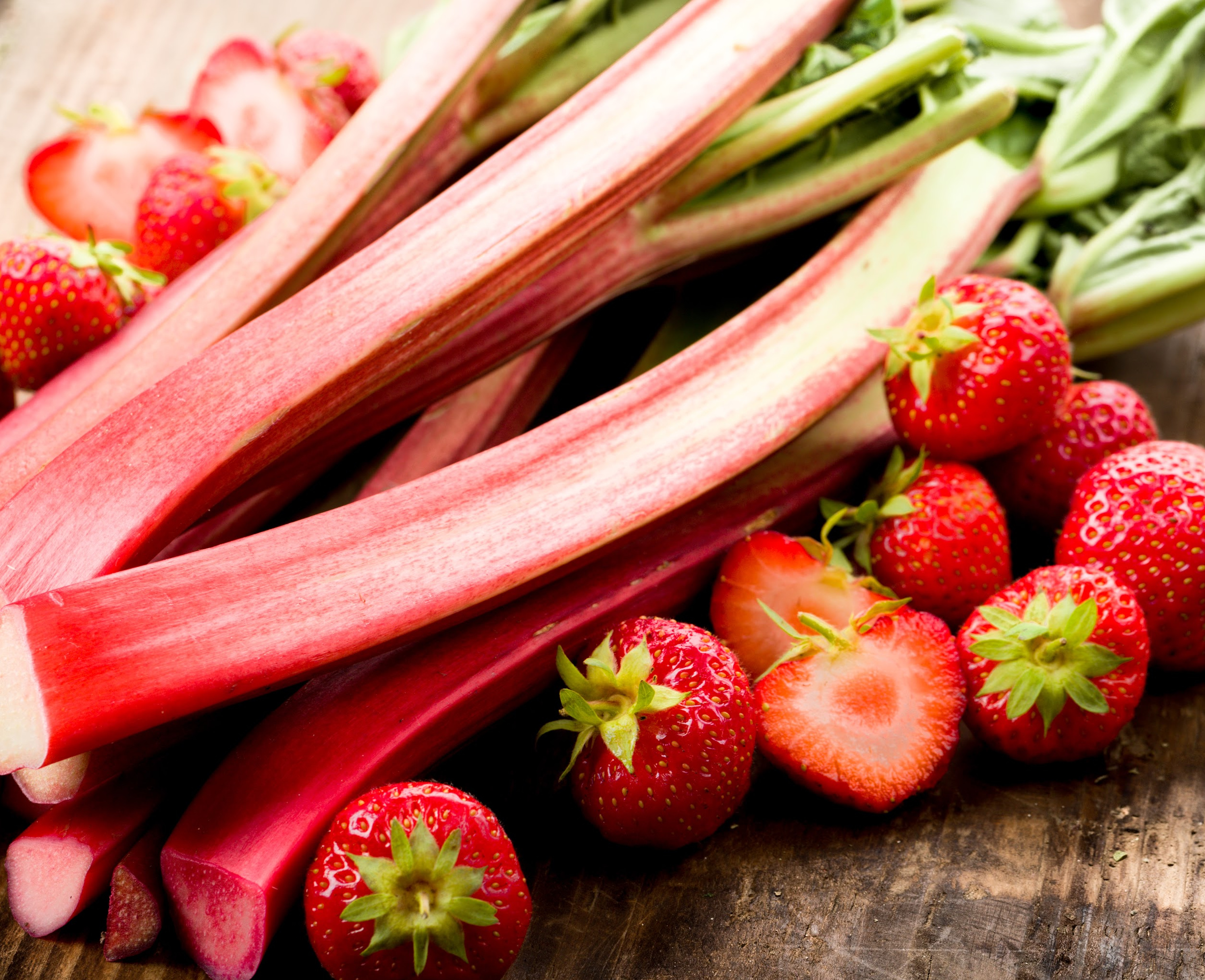 Fresh rhubarb and strawberries on a wooden surface