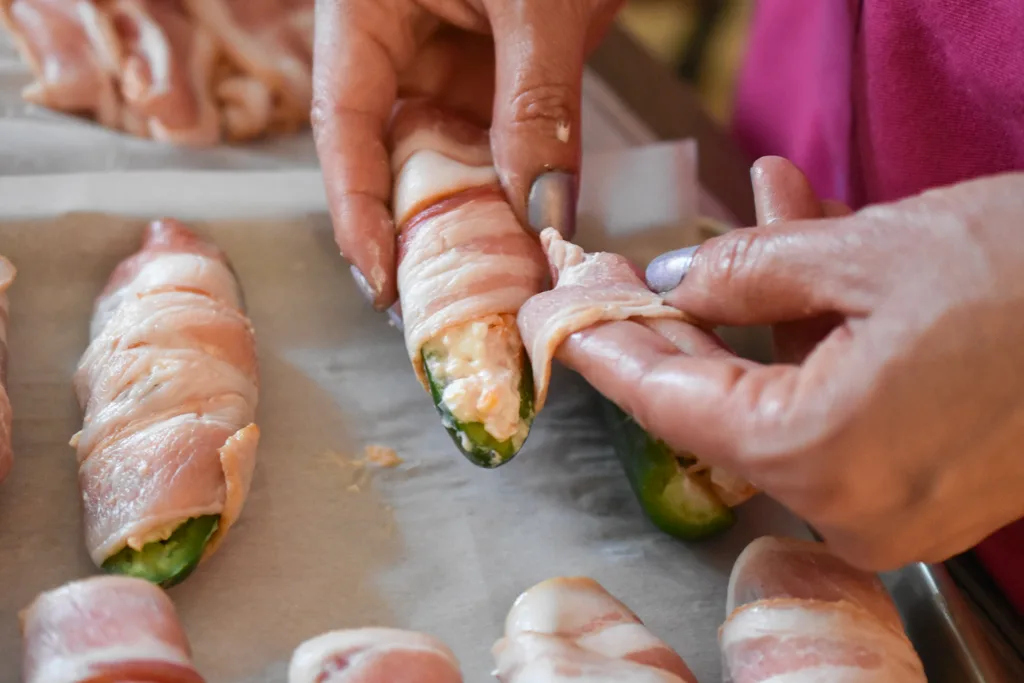 keto roasted jalapeno poppers being wrapped in bacon