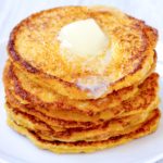 Keto Johnny Cakes stacked on a white plate with a pat of butter melting