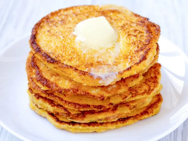 Keto Johnny Cakes stacked on a white plate with a pat of butter melting