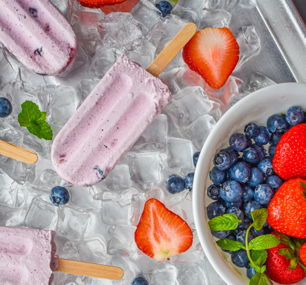 keto berries and cream popsicles on ice and white bowl with berries and mint up close