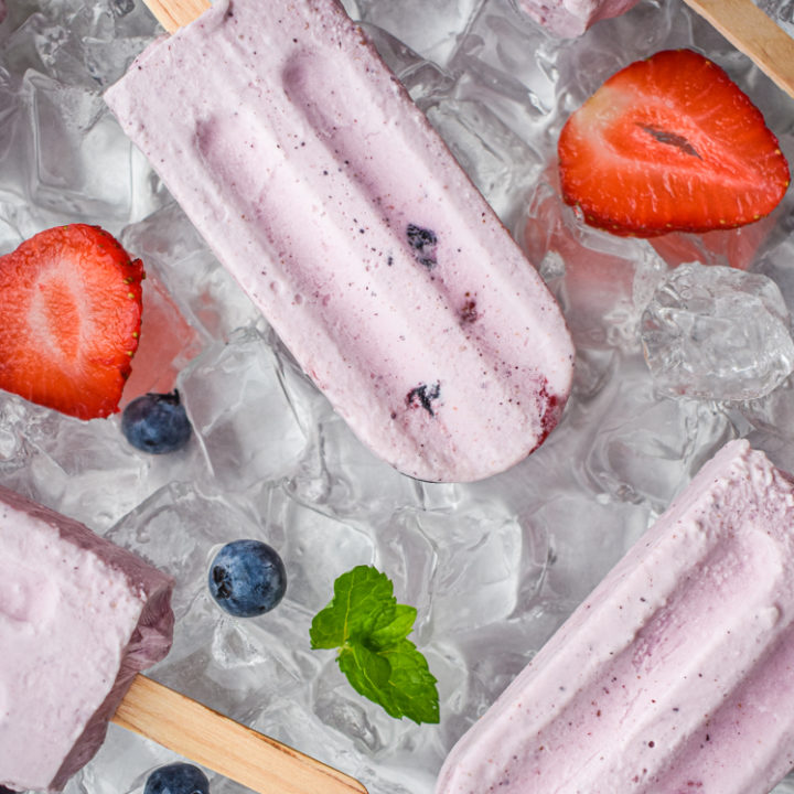 keto berries and cream popsicles on ice with scattered berries on a tray of ice