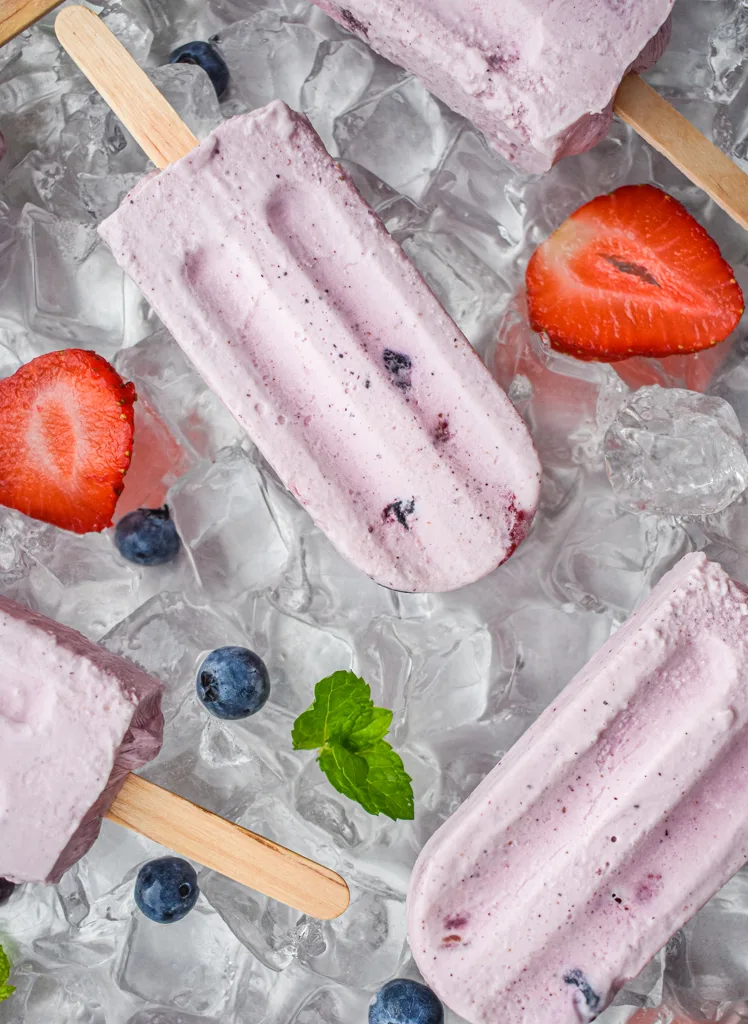 keto berries and cream popsicles on ice with scattered berries on a tray of ice