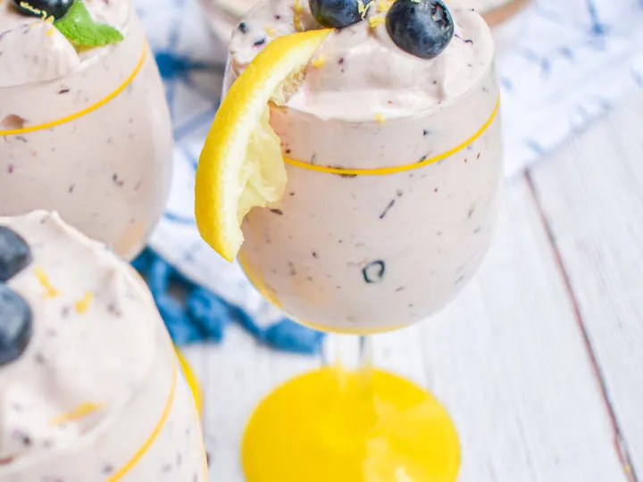 keto blueberry cheesecake mousse in a glass cup with lemon on the rim topped with blueberries and lemon zes