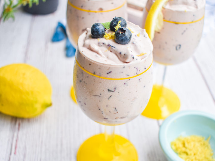 keto blueberry cheesecake mousse in a glass cup with yellow rim and base with lemon in the background