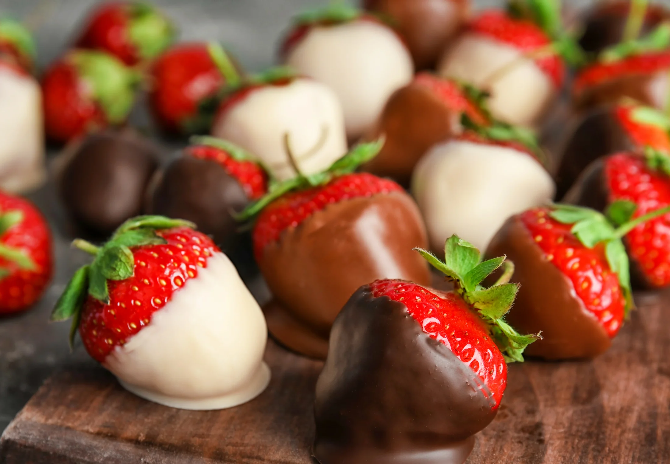 A mixture of keto chocolate covered strawberries in sugar-free dark, milk and white chocolate on a wooden board